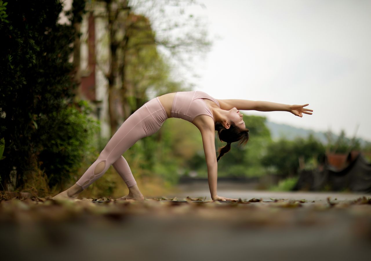 Woman practicing yoga outdoors on a forest road, emphasizing fitness and balance.