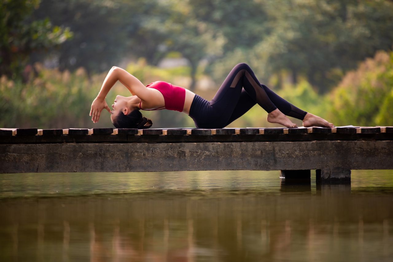 Woman practicing yoga on a serene pier, surrounded by nature. Perfect for wellness themes.