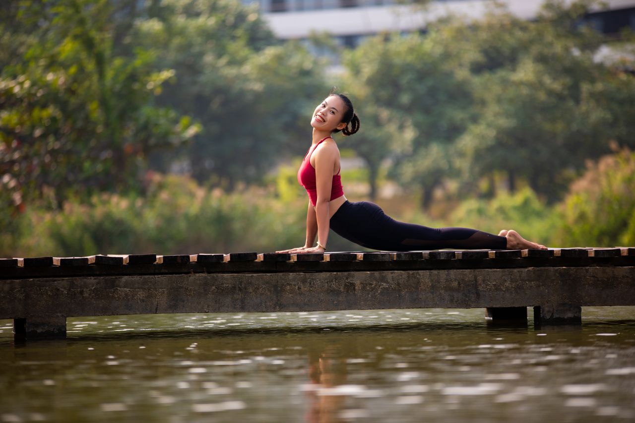 A woman enjoys a yoga pose on a bridge, showcasing flexibility and relaxation in a natural setting.